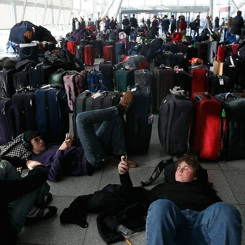 Travelers rest near dozens of suitcases while...