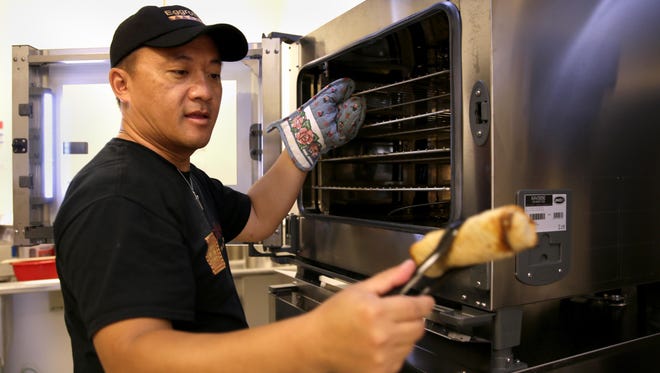 Blong Yang, owner of Eggrolls Inc., takes an egg roll out of the oven before the family-and-friends opening Friday, in Grand Chute, Wis. The restaurant opens to the public Monday.