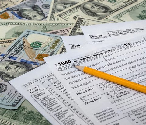 Tax forms on top of a spread-out pile of large-denomination U.S. money.