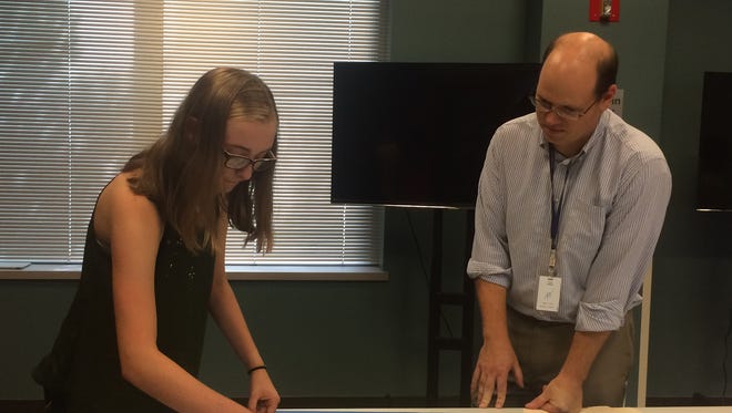 Greg Vadney, director of the Rahr-West Art Museum, helps Maddie Backhaus prepare an intro panel for the library's art exhibit.
