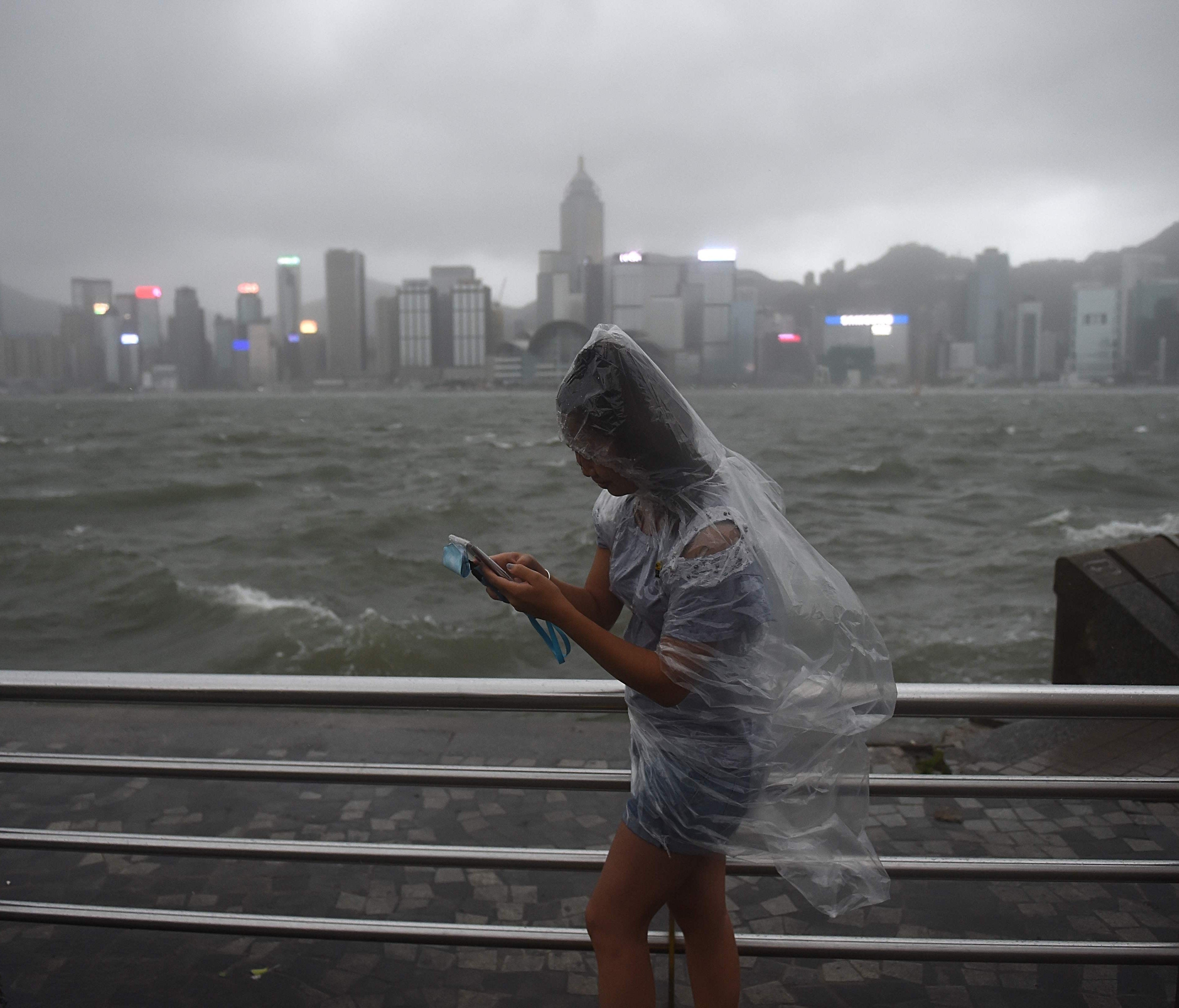 A woman uses her phone while wearing a plastic poncho along Victoria Harbour during heavy winds and rain brought on by Typhoon Hato in Hong Kong on Aug. 23, 2017.  Typhoon Hato smashed into Hong Kong on Aug. 23 with hurricane force winds and heavy rai