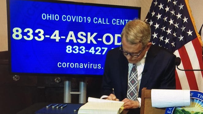 Ohio Gov. Mike DeWine signs a bill enacting emergency measures resulting from the coronavirus pandemic on Friday, March 27, at the Ohio Statehouse in Columbus.
