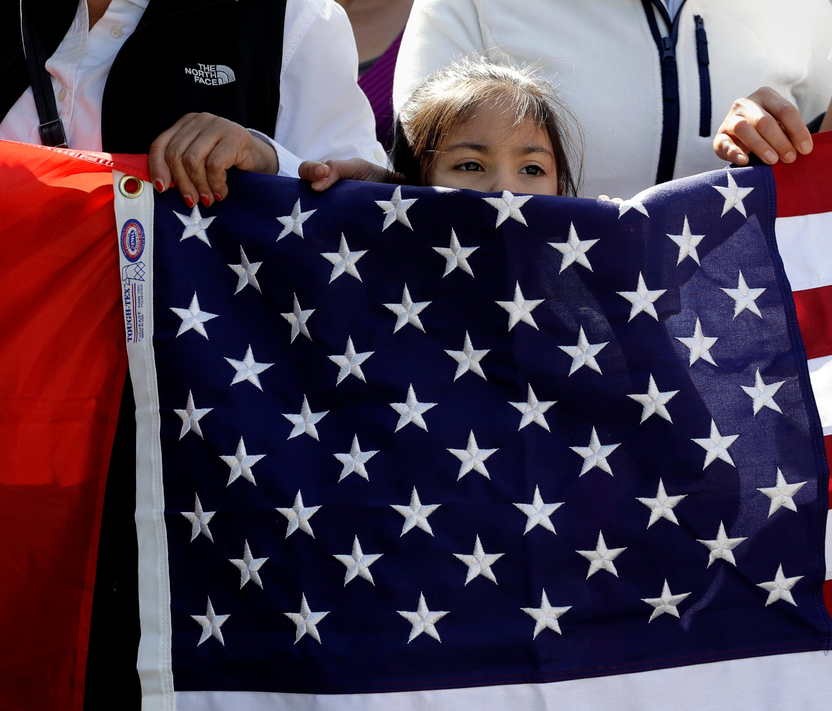 A young girl helps hold a U.S. flag as a group marches through downtown Austin heading to the Texas Capitol during a Day Without Immigrants protest Feb. 16, 2017.