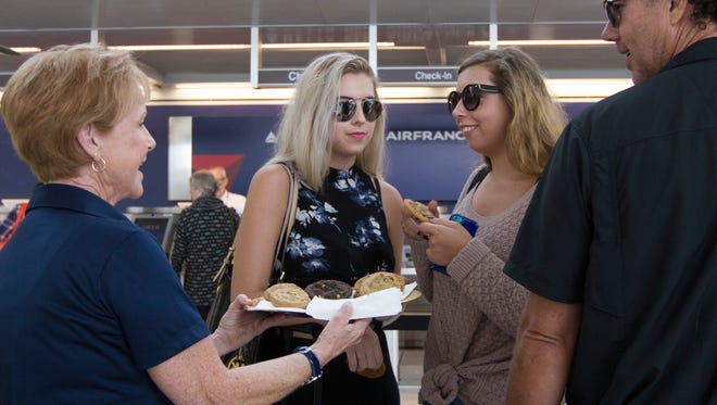 From left, Joyce Morris, a tourism ambassador with the Visitors and Convention Bureau, gives out cookies to travelers Kala, Kasse and Michael Parkinson at the Delta Airlines counter at Southwest Florida Interanational Airport Monday afternoon. Delta Airlines was experiencing worldwide delays due to a technical glitch in their computers system.  Local VCB personnel were in hand to help travelers have a more pleasent experience despite any possible delays.