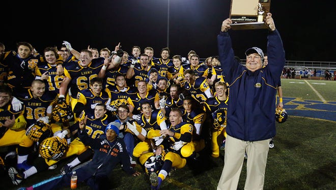 South Lyon coach Mark Thomas holds up the KLAA title trophy as his players wait to pose with the trophy to celebrate their 17-7 win over Canton on Friday in South Lyon.