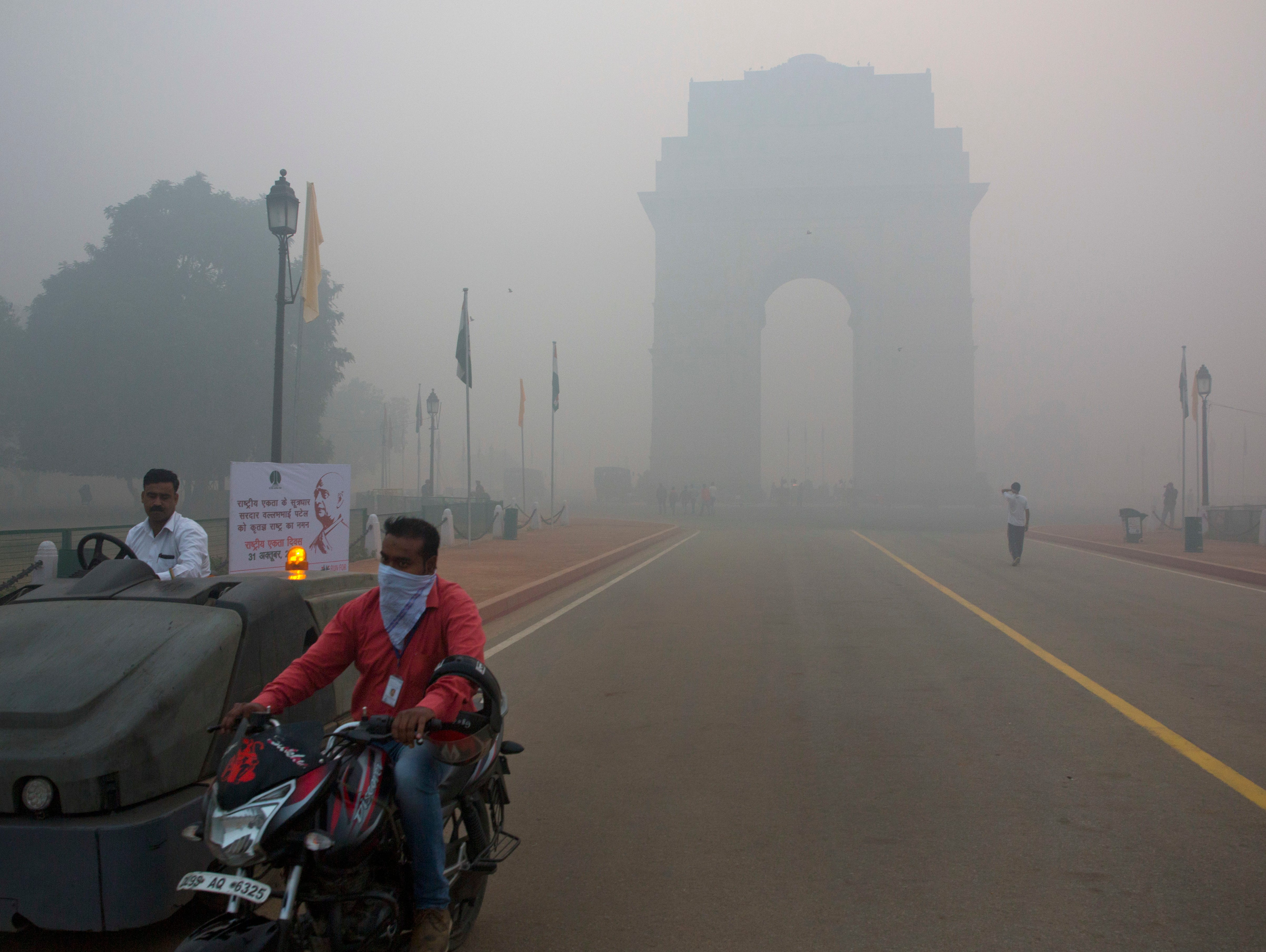 A man covers his face with a scarf as he rides in front of the landmark India Gate, enveloped by smoke and smog, on the morning following Diwali festival in New Delhi, India, Monday, Oct. 31, 2016.