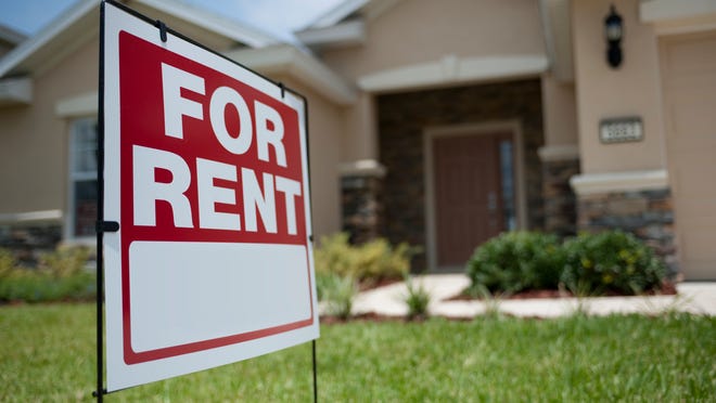 A for-rent sign in the front yard in front of a single-family home.