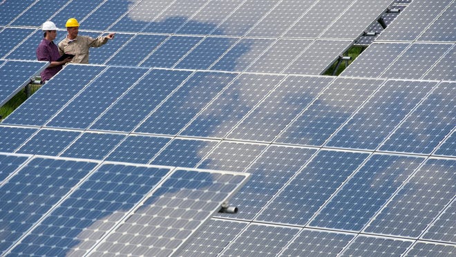 Two engineers stand among an array of solar panels.