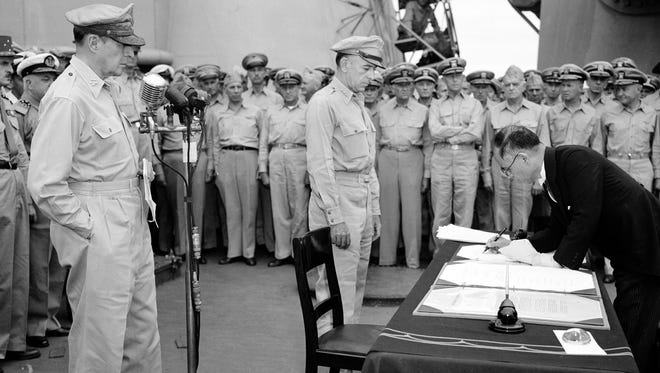 U.S. General Douglas MacArthur, left, watches as the foreign minister Manoru Shigemitsu of Japan signs the surrender document aboard the USS Missouri on Tokyo Bay, Sept. 2, 1945.   Lt. General Richard K. Sutherland, center, witnesses the ceremony marking the end of World War II with other American and British officers in background.