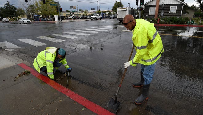 City of Reno Sewer Division employees Dustin Clark, right, and Kelly Petersdorf work to clear a storm drain following a flash flood at the intersection of Sutro and 9th in Reno on July 7, 2015.