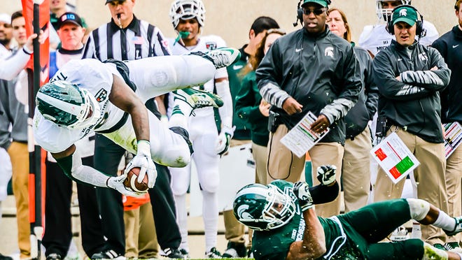 MSU co-defensive coordinators Harlon Barnett and Mike Tressel, background right, watch as Demetrious Cox upends Lawrence Thomas during Saturday’s spring game at Spartan Stadium. Spring practices are a time for teams to assess players’ skills and roles. Cox is battling for a starting position this fall at either cornerback or safety, while defensive lineman Thomas was being used as a fullback on the play during the scrimmage.