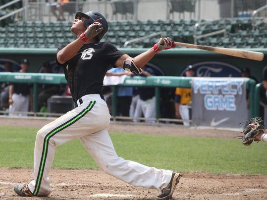 a man in a dark green baseball shirt swings a baseball bat in a stadium