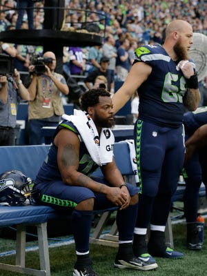 Seattle Seahawks center Justin Britt, right, stands next to defensive end Michael Bennett as Bennett sits on the bench during the singing of the national anthem before the team's NFL football preseason game against the Minnesota Vikings.