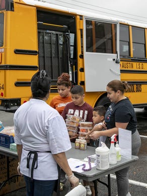 Families pick up their free breakfast and lunch that was delivered on a school bus to Park Place at Loyola apartments in late March. The Austin district continue to provide free meals to its students and their parents, including on weekends, amid the school closures caused by the coronavirus pandemic.