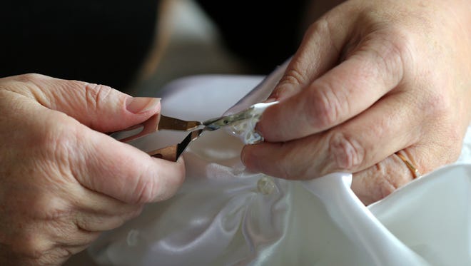 Pearls and needing are removed from a used wedding dress. The dress material is then used to make infant burial gowns and donated to area hospitals. 