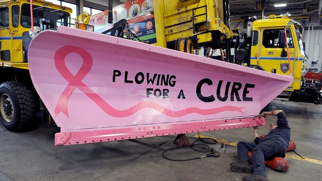 Framingham DPW Mechanic Mike Bond attaches the final bolts to one of two pink snow plows attached to all-wheel drive Oshkosh Snow Fighter trucks for Breast Cancer Awareness Month.