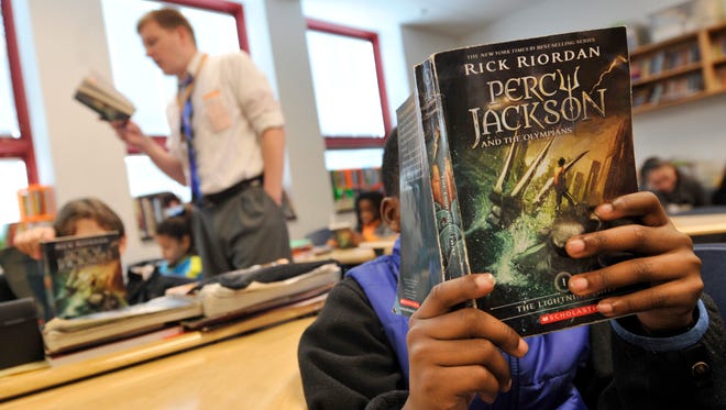 Tebyus Peyton, a fifth grader at Jackson K-8 school, reads along with his teacher Jonas Lau, rear, as the class works through another chapter of "Percy Jackson." York City School District's revised recovery plan focuses on infrastructure, including rewriting the math and English language arts curriculum.