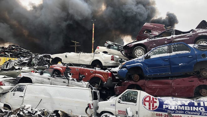 Black smoke rises above a pile of junked vehicles as Detroit firefighters battle a blaze at a scrapyard on Detroit's east side.