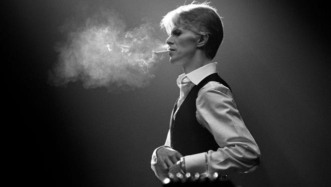David Bowie lights a cigarette during a performance at a show on the Isolar tour in support of his 'Station to Station' album. 1976.