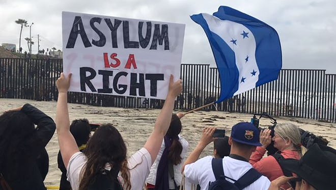 Central American migrants and supporters of the migrant caravan hold up signs from the U.S. side of the border looking south into Mexico on Sunday, April 29, 2018.