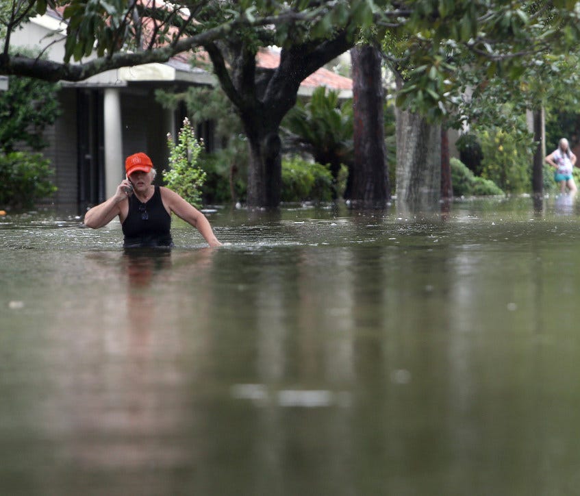 A man talks on his phone as he wades along a flooded Meyerland street, Sunday, Aug. 27, 2017, in Houston. Cell-phone drying companies were offering free services to customers whose water-logged phones were inoperable.