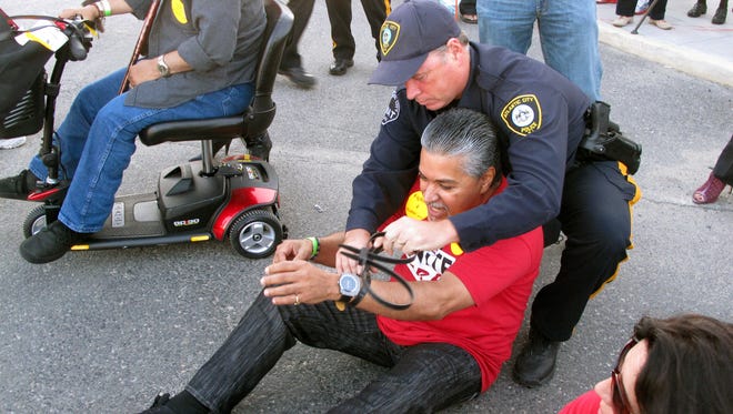 An Atlantic City officer arrests a demonstrator in Wednesday’s protest by the Unite-HERE union over a demand by the Trump Taj Mahal’s owner to cut health and pension benefits. Police arrest a protester sitting in a roadway in Atlantic City N.J. during a demonstration on Wednesday, Oct. 8, 2014. They were protesting givebacks demanded by the owners of the Trump Taj Mahal Casino Resort in return for keeping the casino open. The company wants to eliminate employee health care and pension plans. Twenty four of the workers were arrested in the protest.