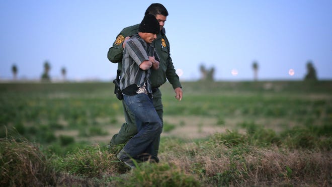 
A Customs and Border Patrol officer walks with an apprehended undocumented immigrant from Guatemala who was found hiding in the tall grass just south of the border wall near Weslaco, Texas. 

