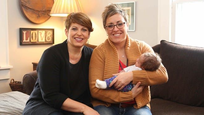 Jackie and Lisa Phillips-Stackman hold their daughter, Lola, at their Indianapolis home, Friday, Dec. 4, 2015. The couple are filing a lawsuit against the state to try to get Indiana to recognize both same-sex parents on their children's birth certificates.