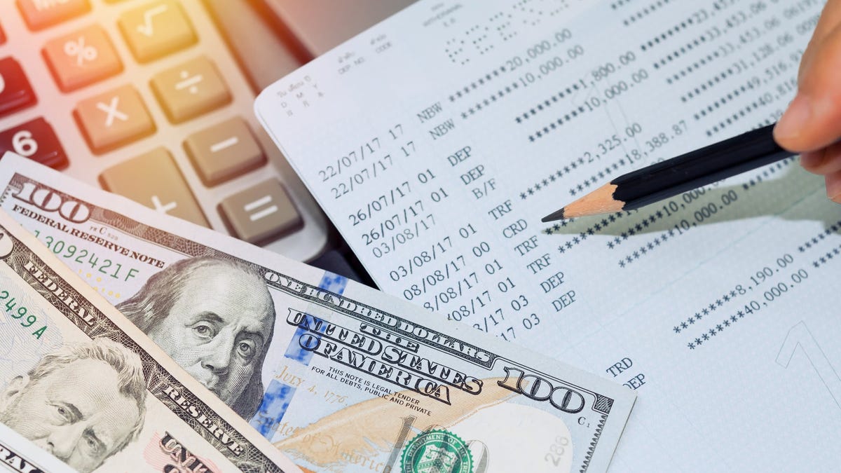 Savings passbook with pencil, calculator, and cash on a flat surface.