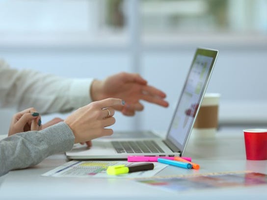 Hands pointed toward laptop screen with papers and highlighters next to it