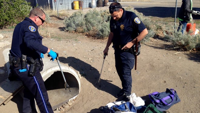 Reno Police Officers Jason Stallcop and Cameron Green pull clothing, blankets and bags from a concrete drain Friday morning near the entrance of Fisherman's Park.