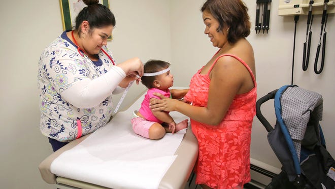 Medical assistant Josefina Gutierrez (left) takes a head measurement from 1-year-old Andrea Vasurto as her mother, Gabrielle Vasurto, keeps her daughter occupied during her  physical at the Sixteenth Street Community Health Center clinic on 16th St. in Milwaukee in 2015.
