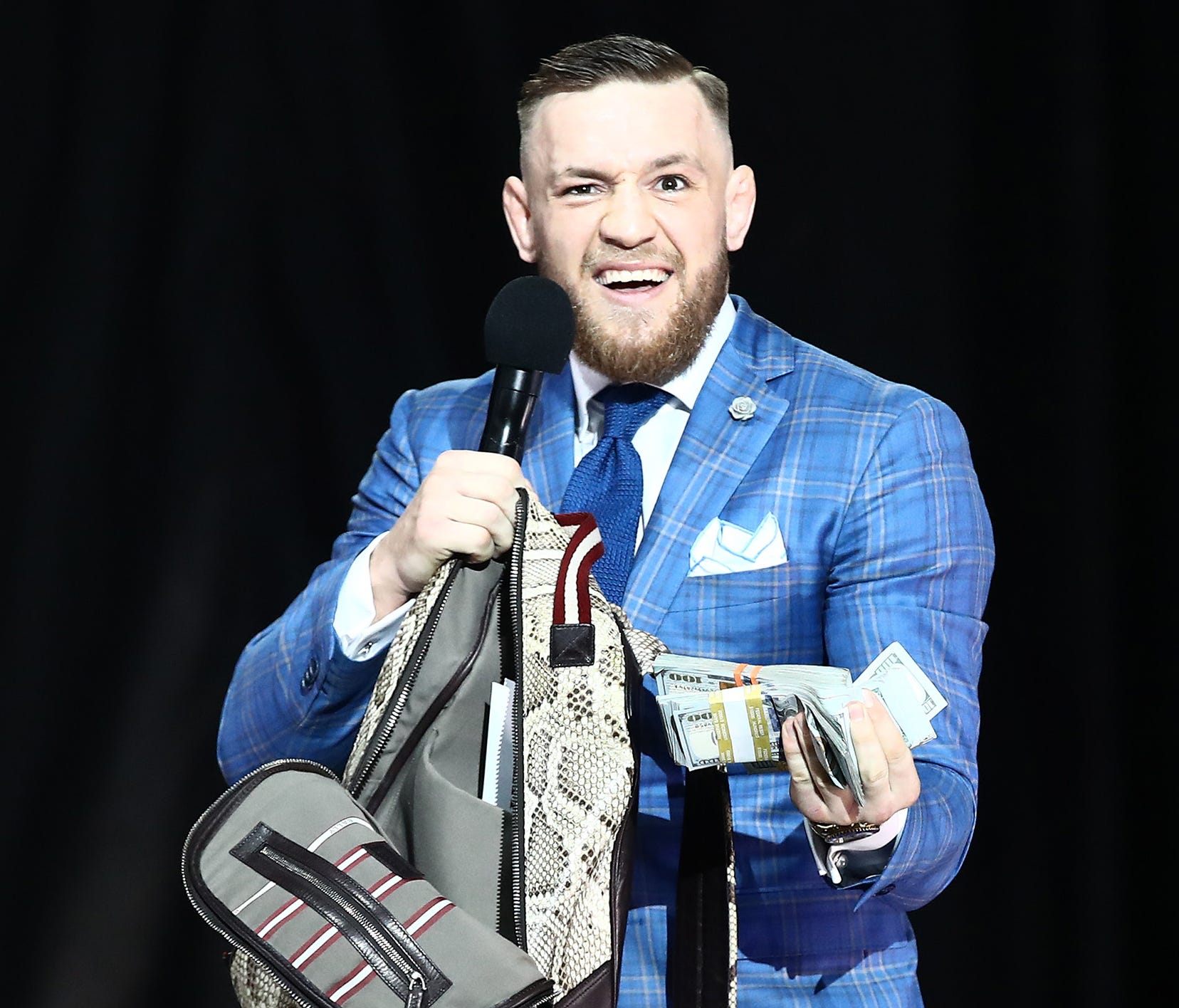 Conor McGregor reacts as he takes cash from a money bag brought onto the stage by Floyd Mayweather during a world tour press conference to promote the Mayweather vs. McGregor fight.