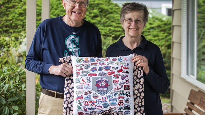 Jim and Andrea Siscel have visited 323 baeball parks since 2002, making a trip every year, but had to cancel this year's adventure because of COVID-19. At home in Lynnwood, Washington, on July 9, 2020, they are holding a T-shirt, made into a pillow, with minor league stadiums printed all over it.