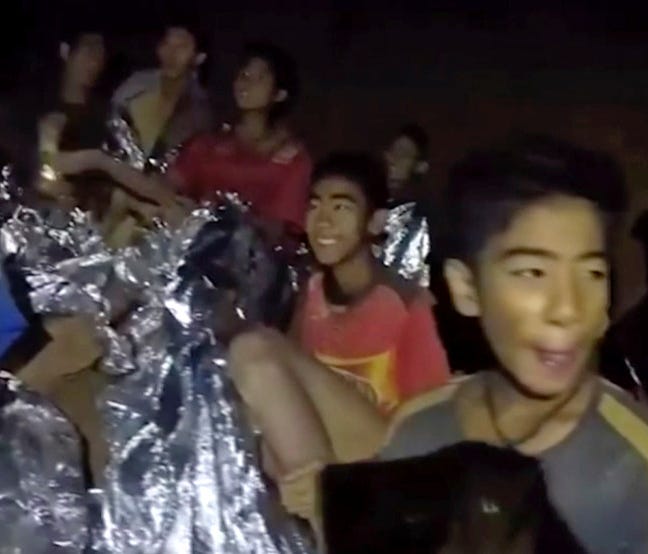 In this July 3, 2018, image taken from video provided by the Royal Thai Navy Facebook Page, a Thai boy smiles as a Thai Navy SEAL medic helps injured children inside a cave in Mae Sai, northern Thailand.