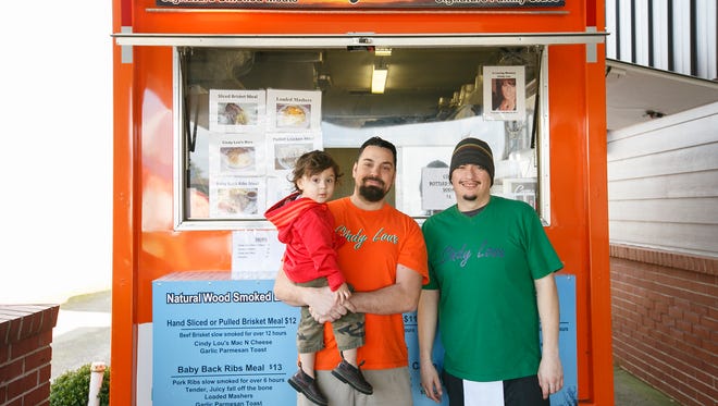 Johnny Roldan (from right) and David Sarff, holding his son Xavier, stand in front of the Cindy Lou BBQ cart on Lancaster Drive. Roldan is the pitmaster, and Sarff's cousin, Christopher, owns the cart.