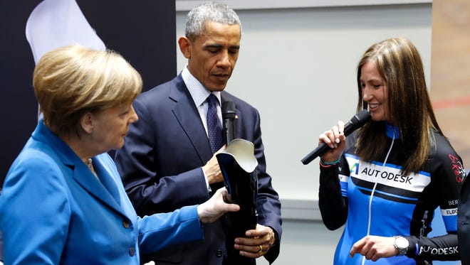 German Chancellor Angela Merkel (L) holds a custom-fit leg prosthesis as she and President Barack Obama (C) chat with German Para-cycling world champion Denise Schindler at the Autodesk booth on April 25.