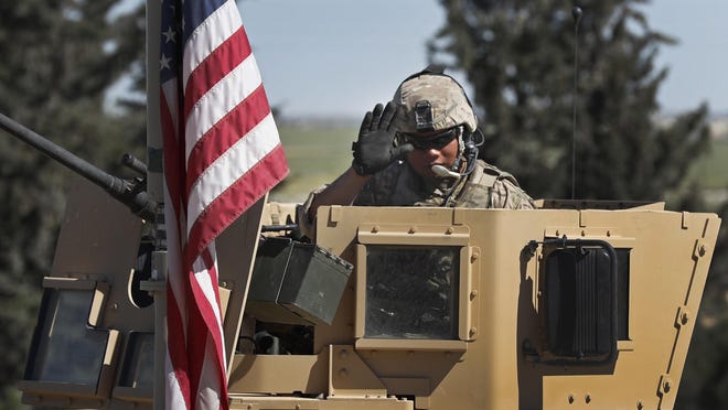 In this April 4, 2018 photo, a U.S. soldier waves as he sits on an armored vehicle, at a road leading to the tense front line with Turkish-backed fighters, in Manbij town, north Syria. President Donald Trump's decision to withdraw troops from Syria has rattled Washington's Kurdish allies, who are its most reliable partner in Syria and among the most effective ground forces battling the Islamic State group. Kurds in northern Syria said commanders and fighters met into the night, discussing their response to the surprise announcement Wednesday, Dec. 20, 2018. (AP Photo/Hussein Malla)