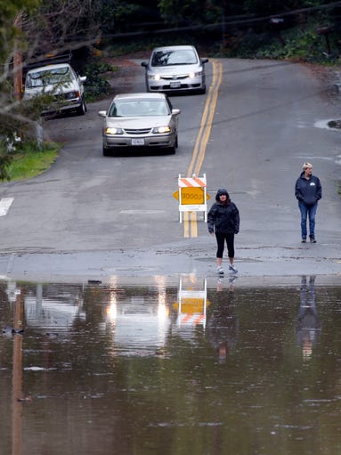 Residents stand at the edge of a road flooded due to