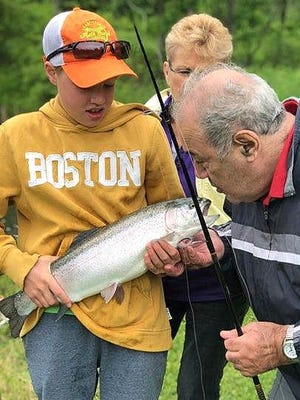 Volunteer Benjamin Swinnerton, 14, holds a rainbow trout caught by Frank LaVore during the recent Finger Lakes Fishing Preserve VIP tournament.