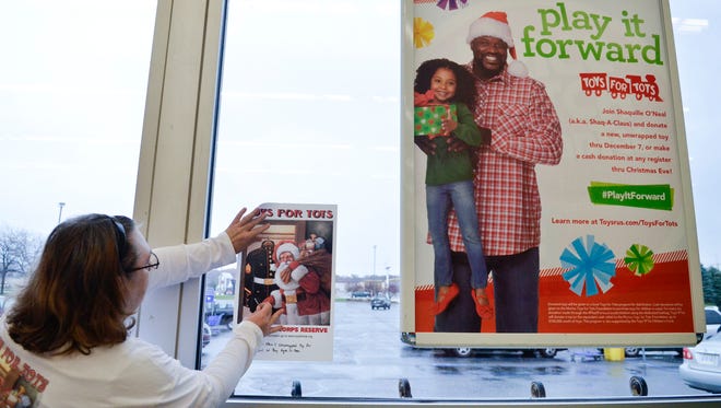 Connie Melvin, of Kimball Township, tapes a poster onto the window over the drop box for St. Clair County Toys for Tots at the Fort Gratiot Toy “R” Us. Melvin has been a volunteer for 26 years with Toys for Tots.