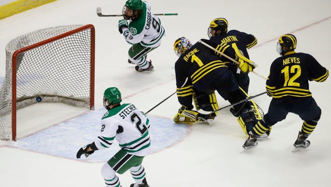 North Dakota's Drake Caggiula (9) scores on Michigan goalie Steve Racine (1) as Michigan's Cutler Martin, second from right, and Cristoval Nieves (12) and North Dakota's Troy Stecher (2) watch during the first period of the Midwest Regional final of the men's NCAA college hockey tournament, Saturday, March 26, 2016, in Cincinnati.