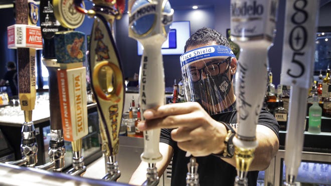 A bartender pours a beer while wearing a mask and face shield amid the coronavirus pandemic at Slater's 50/50 Wednesday, July 1, 2020, in Santa Clarita, Calif. According to a new poll, Americans overwhelmingly are in favor of requiring people to wear masks around other people outside their homes, reflecting fresh alarm over spiking infection rates. The poll also shows increasing disapproval of the federal government's response to the pandemic. California is among the states seeing the greatest surge in cases now.