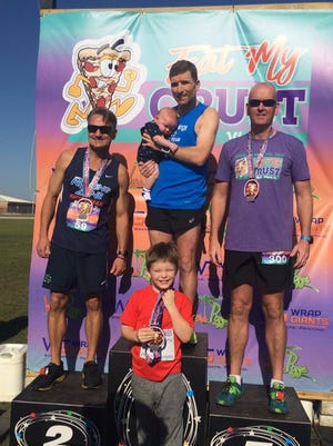 John Wall holds son George with other son Alex in front after winning his age group at the Eat My Crust 5K.