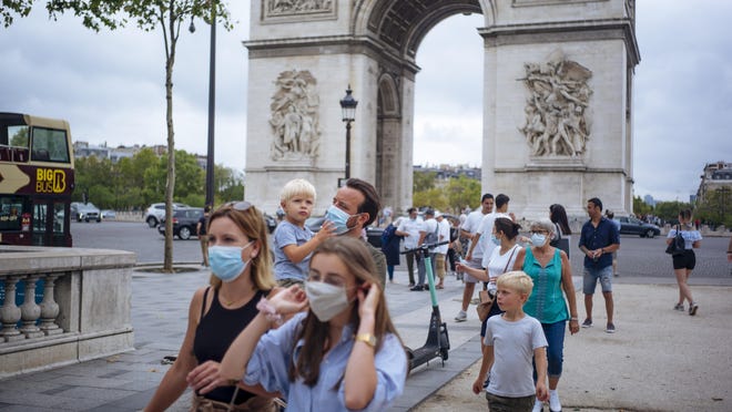 A family wearing protective face masks walk along on the Champs Elysee avenue, with Arc de Triomphe in background, in Paris, Saturday, Aug. 15, 2020. Paris extended the areas of the city where pedestrians will be obliged to wear masks starting Saturday morning after health officials said that the coronavirus is "active". The Champs-Elysees Avenue and the neighbourhood around the Louvre Museum are among zones where masks will be obligatory.