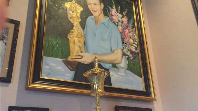 A painting of Arnold Palmer holding the 1954 U.S. Amateur trophy rises above the trophy itself at Arnold Palmer's Resraurant in La Quinta