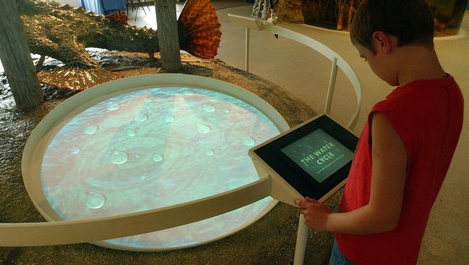 A boy selects an educational film to be projected onto the circular screen on the floor in the lobby of the Environmental Learning Center at Rookery Bay Natural Estuarine Reserve in Naples.