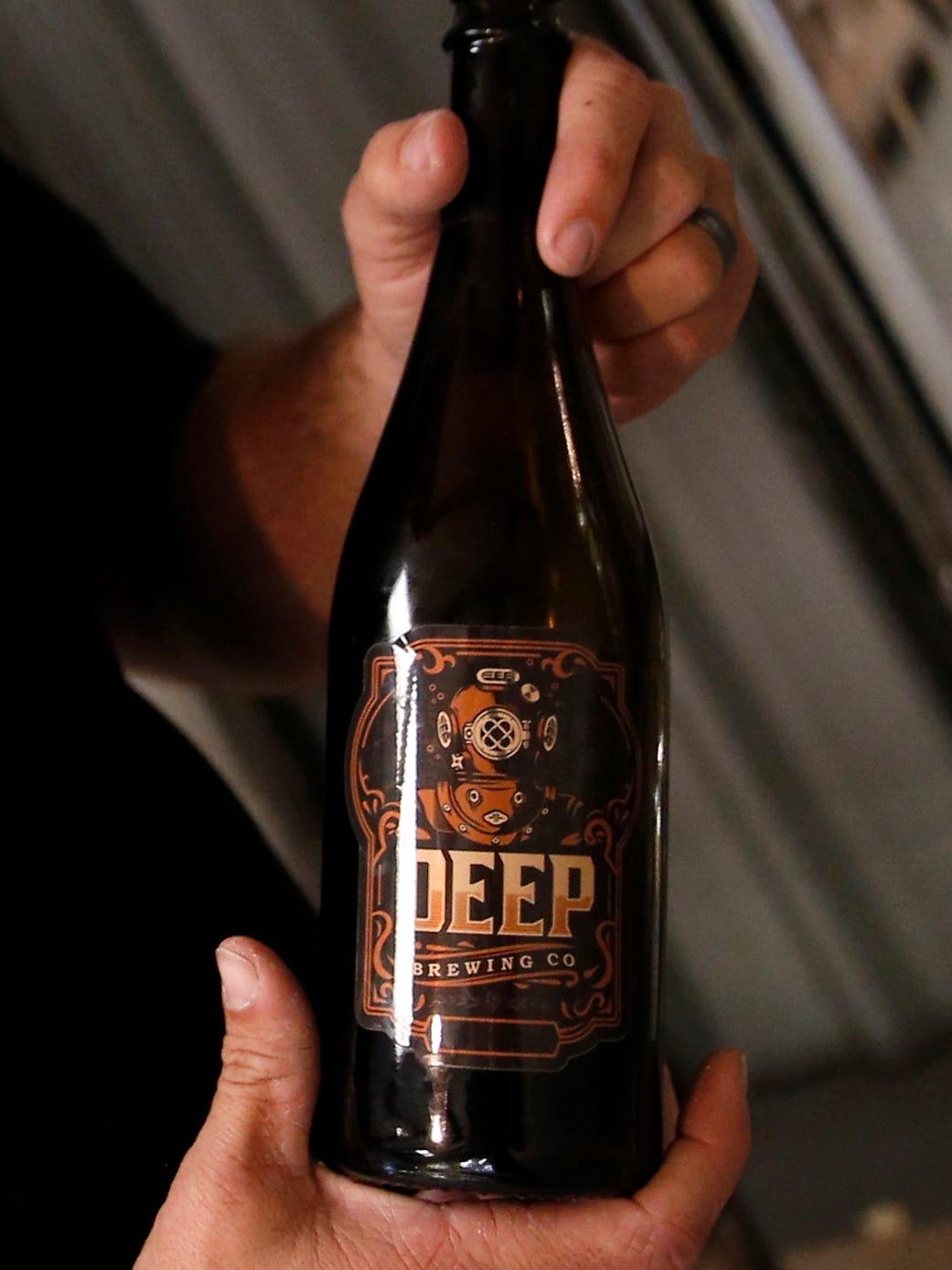 Ryan LaPete, holds one of his Deep Brewing Co. bottles inside his brewery.