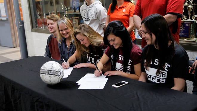Aztec's Grace Olson, center, and Alycea Aviles, right, sign with the New Mexico State women's soccer team during a ceremony on Wednesday.