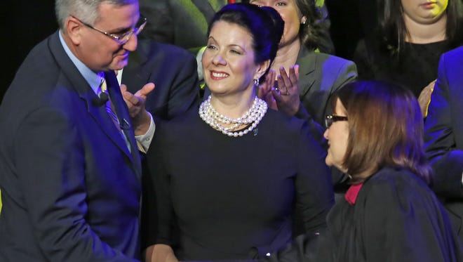 Janet Holcomb, center, smiles as her husband, Eric Holcomb shakes hands with Chief Justice Loretta Rush after being sworn in as governor at the Indiana State Fairgrounds on Monday.